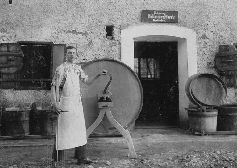 Ein Mann steht vor einem Gerät, das für die Käseproduktion benötigt wurde vor dem alten Gebäude der Firma WOERLE. Ein Foto in schwarzweiß