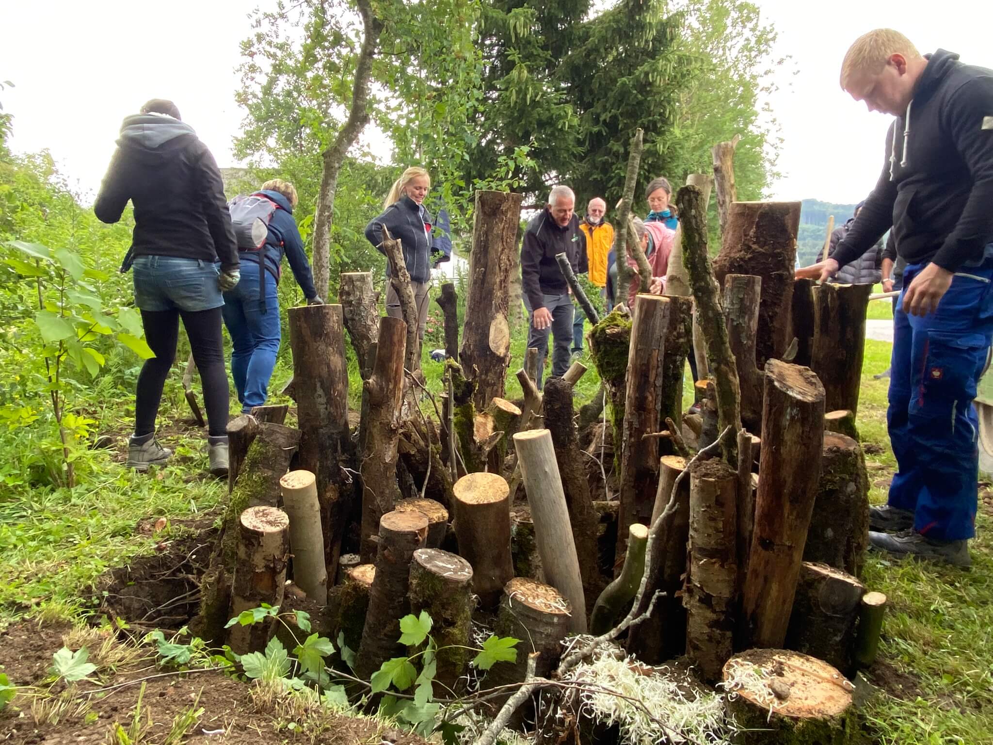 Menschen bauen eine Käferburg, die aus Baumstämmen und Ästen besteht, im Wald ,im Zuge des Projekts Praxiswerkstatt wir bauen eine Käferburg der Firma WOERLE
