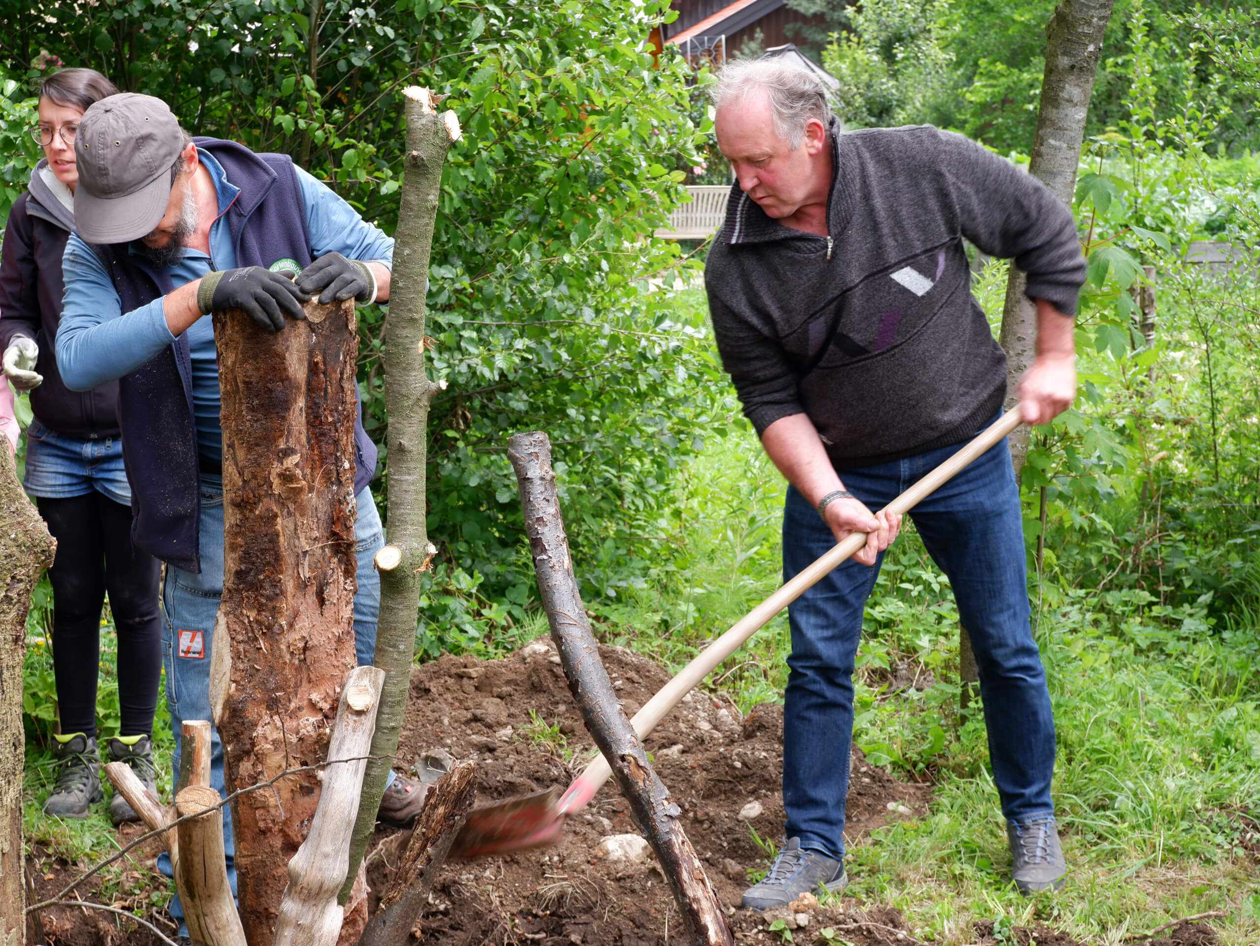 Zwei Männer arbeiten an einer Käferburg im Wald, die aus Baumstämmen und Stöcken besteht. Dies tun sie im Rahmen des Projekts Praxiswerkstatt wir bauen eine Käferburg der Firma WOERLE