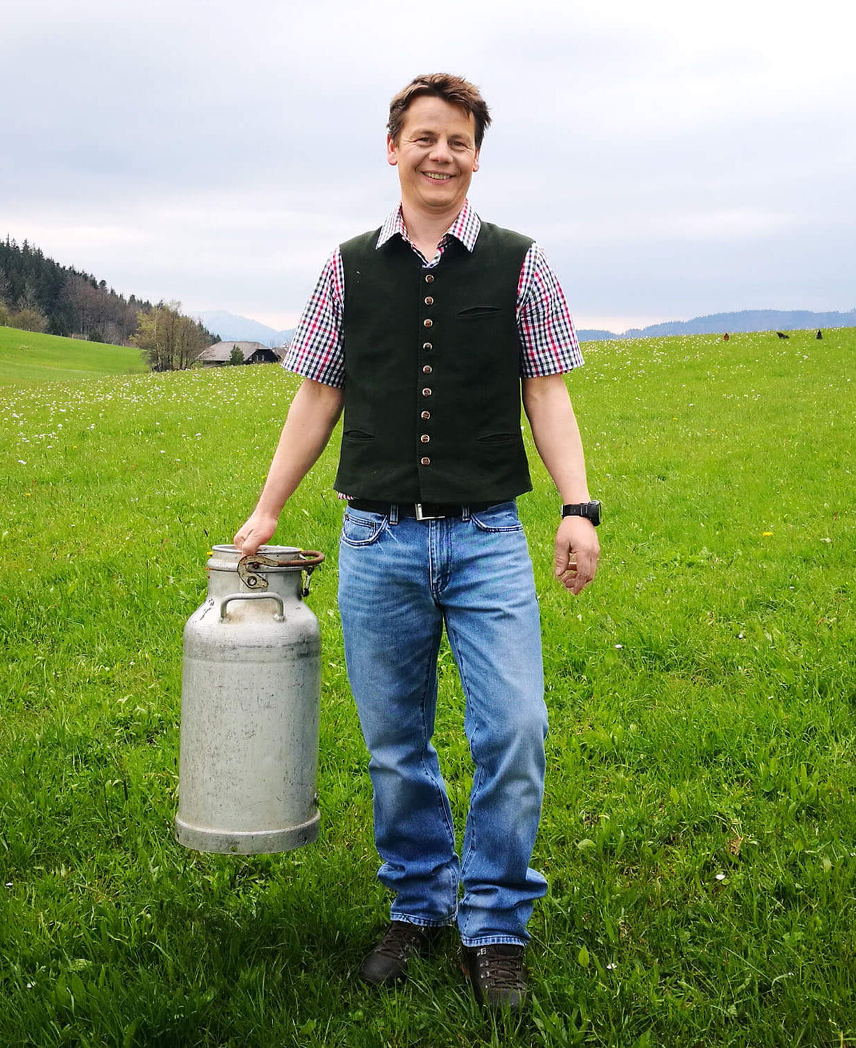 Heumilchbauer auf Wiese mit Milchkanne in der Hand