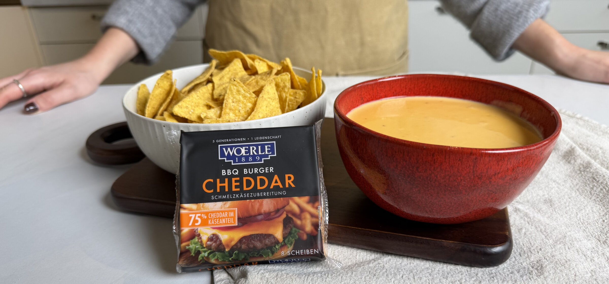 Cremiger Käsedip in roter Schale, daneben Tortilla-Chips und WOERLE BBQ Burger Cheddar Scheiben.